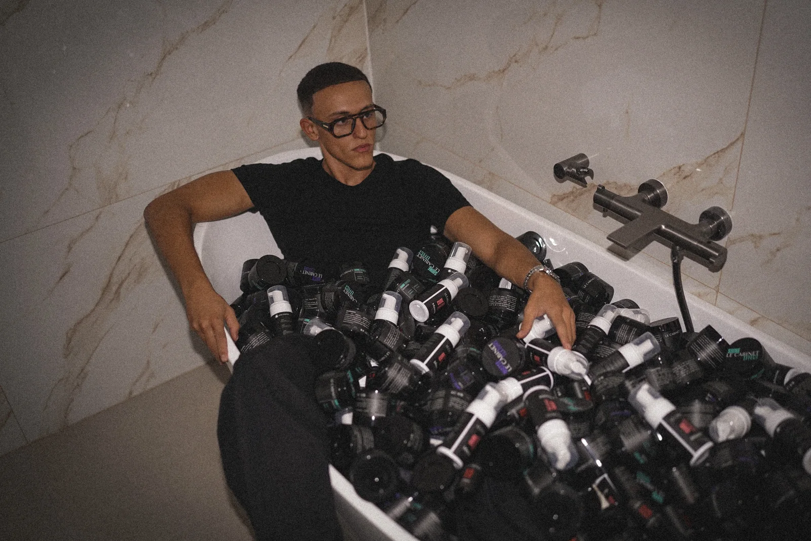 Mehdi entouré de produits, dans la baignoire.